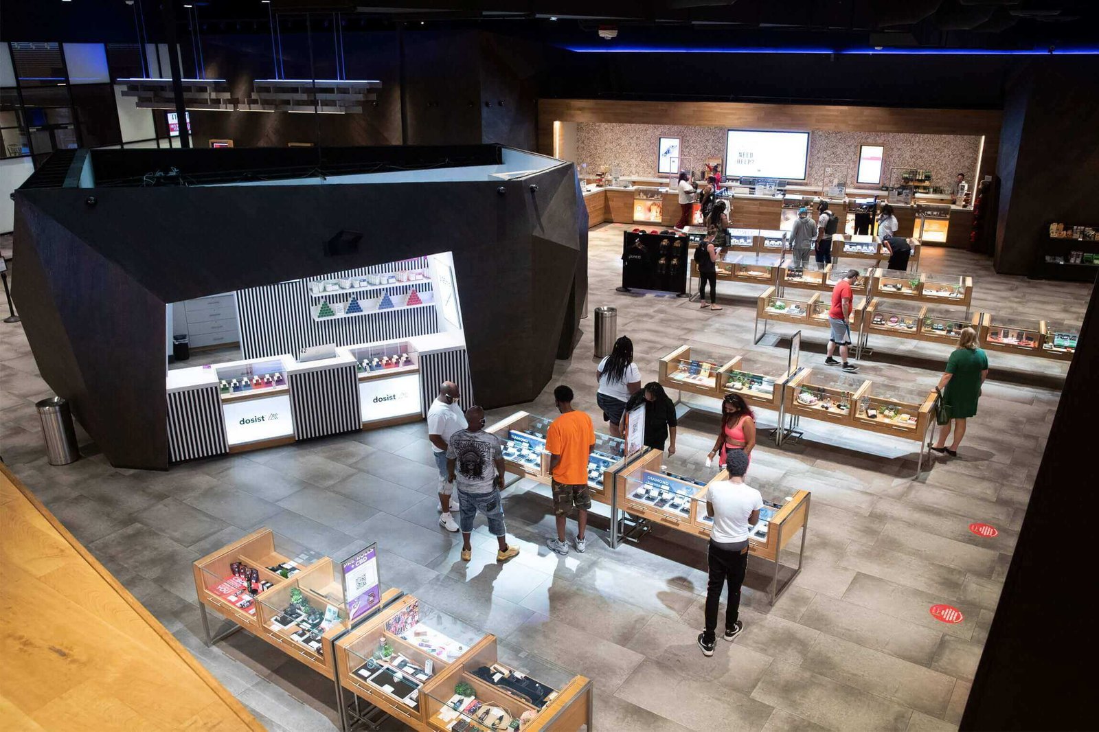 Elevated view of spacious dispensary sales floor with hexagonal central kiosk and customers browsing cases