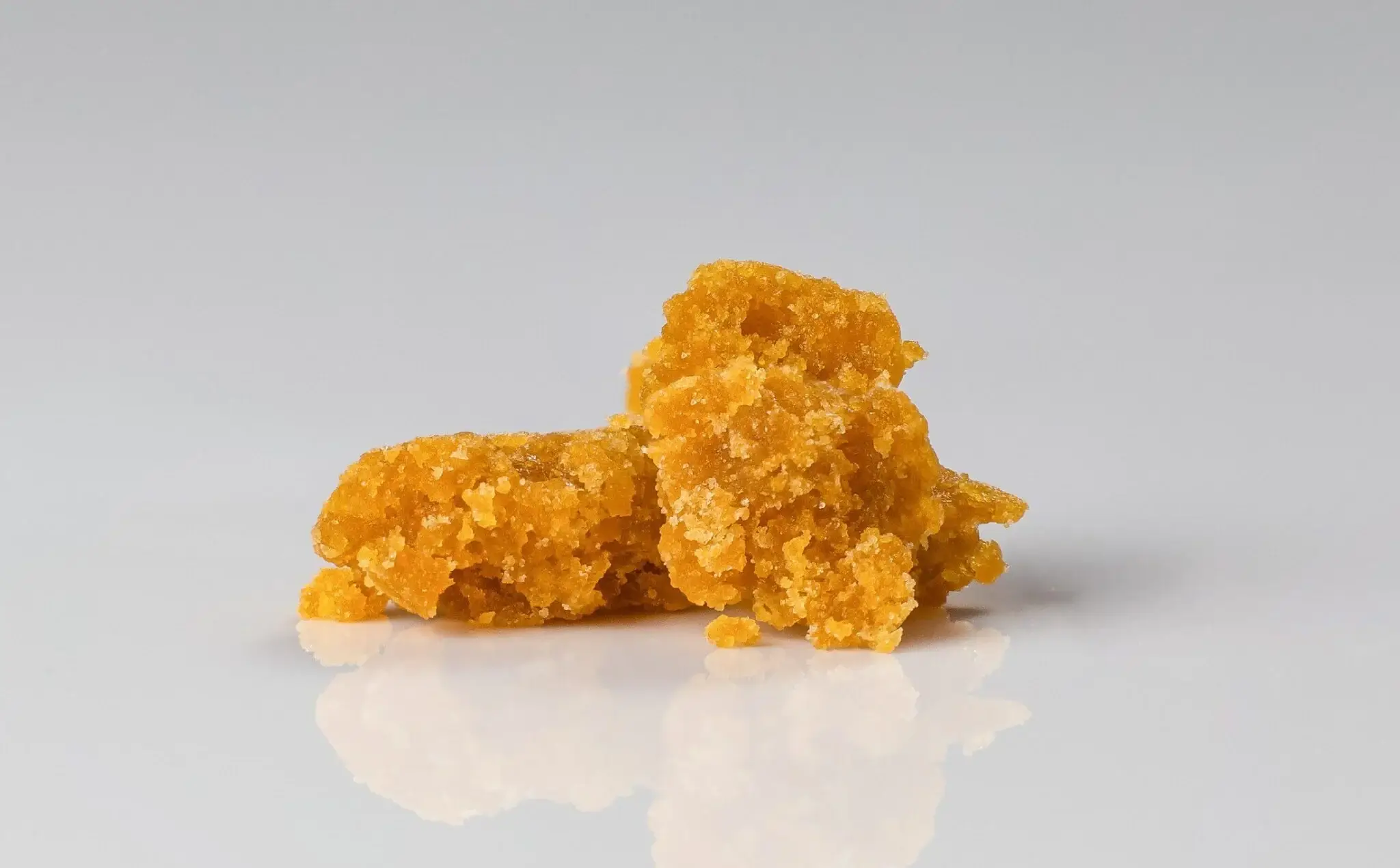 Two pieces of golden orange cannabis crumble wax concentrate on a glossy white surface