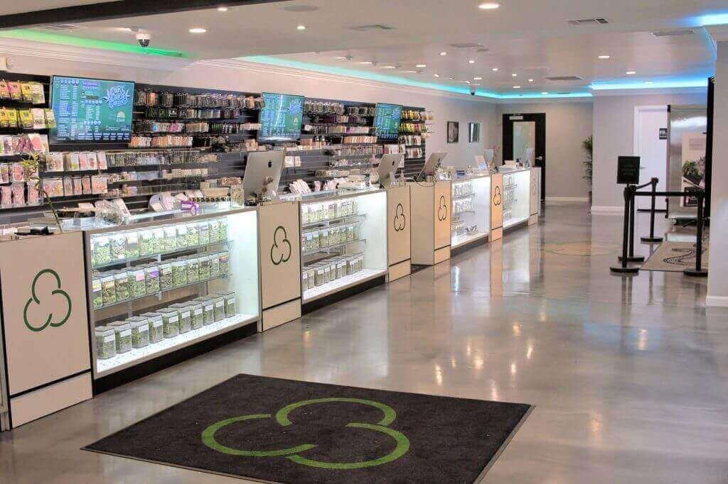 Bright modern dispensary interior with white counters, jar shelves, and floor mat with green logo