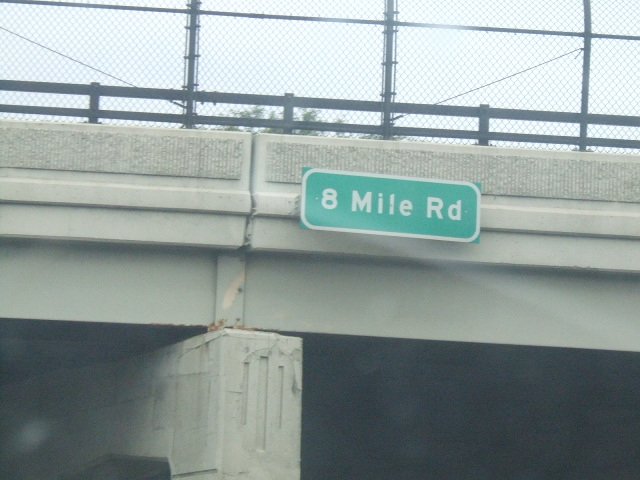 Green 8 Mile Road street sign mounted on a concrete highway overpass over Interstate 94 in metro Detroit