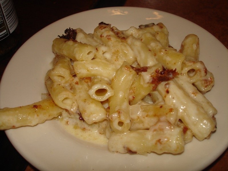 Closeup of a wooden spoon lifting a stretchy cheesy bite of macaroni and cheese from the dish