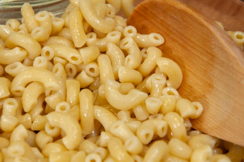 Pile of plain cooked elbow macaroni pasta drained with a wooden spoon