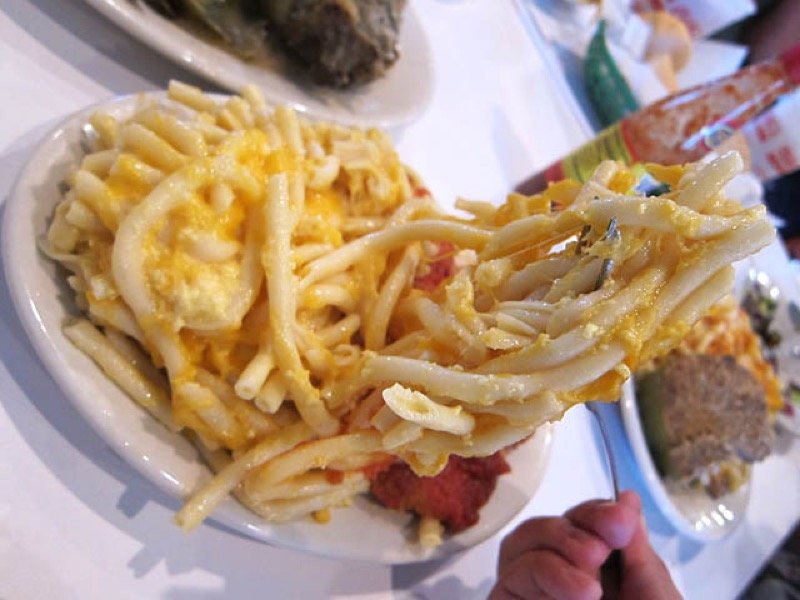 Plated serving of baked macaroni and cheese on a white plate with cheddar pulls