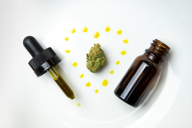 Amber glass dropper bottle of cannabis tincture next to cannabis leaves on a white plate