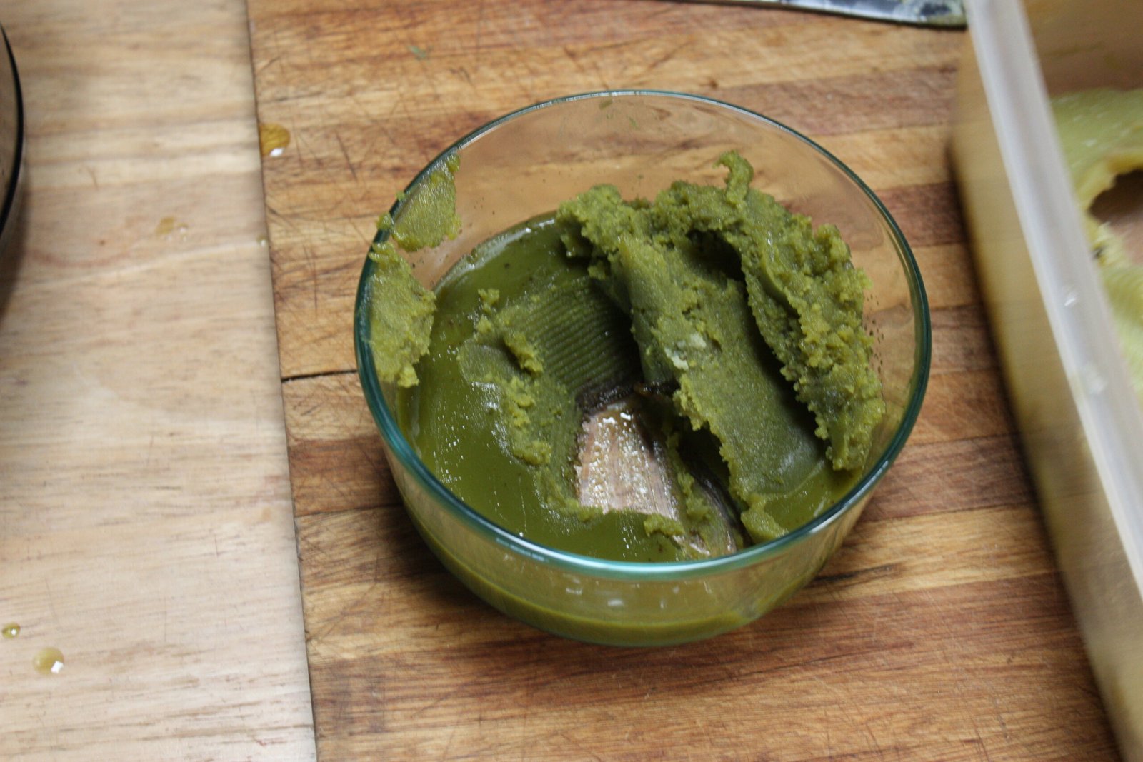 Bright green over-extracted cannabis butter in a glass bowl, the result of squeezing cheesecloth and overheating, an example of what to avoid