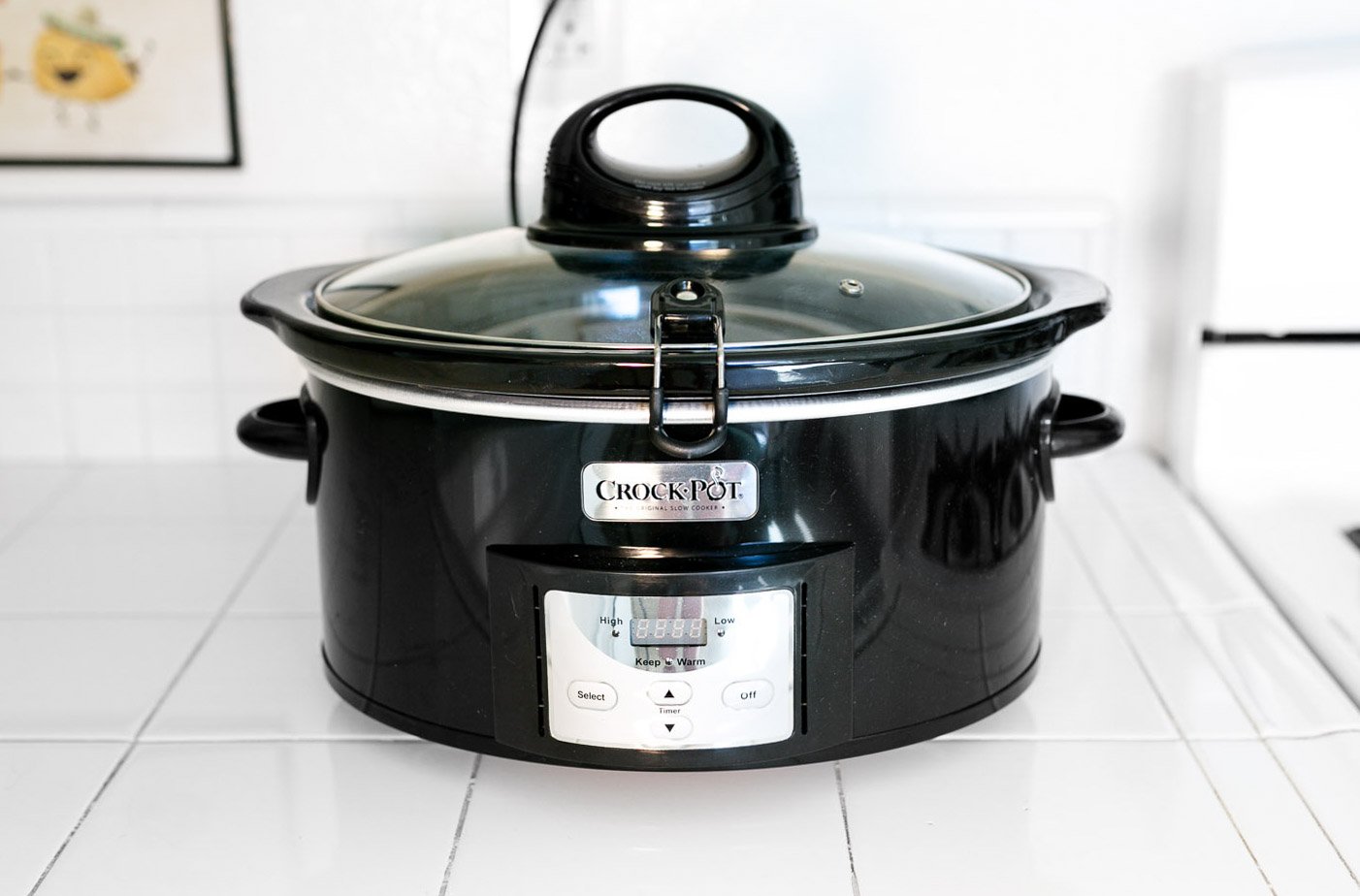 Crock-Pot brand black 6-quart slow cooker on white tile counter with the digital control panel showing High and Low settings