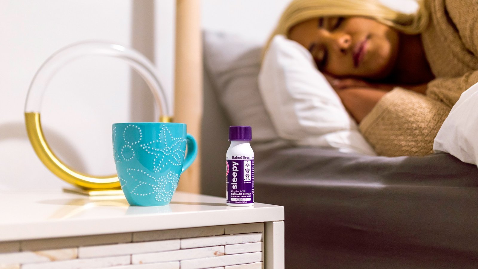 Baked Bros Sleepy King Louie XIII THC infused syrup bottle on bedside table with sleeping woman in background