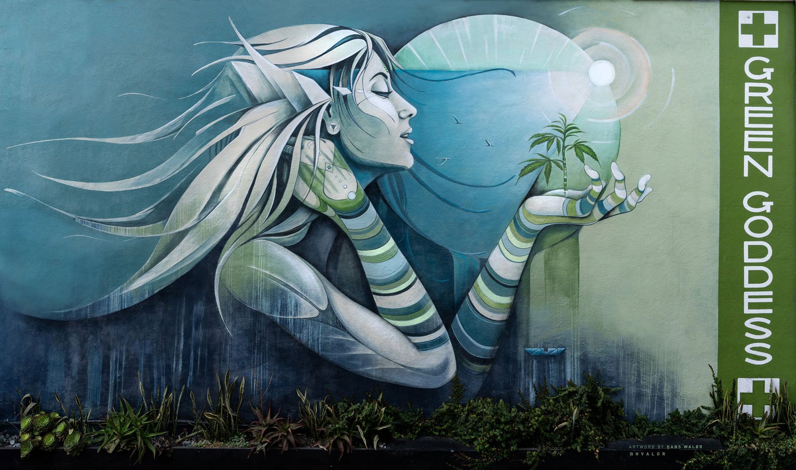 Green Goddess Collective Venice Beach mural by artist Sand Walor showing a goddess holding a cannabis plant, with the Green Goddess vertical sign on the side
