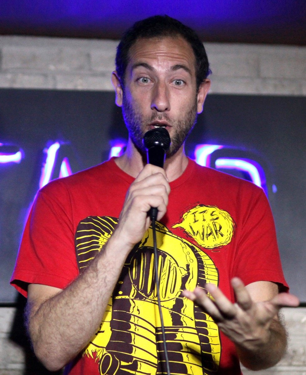 Stand-up comedian Ari Shaffir on stage in a red t-shirt, the loose-cannon long-form cannabis storyteller and Skeptic Tank podcaster.