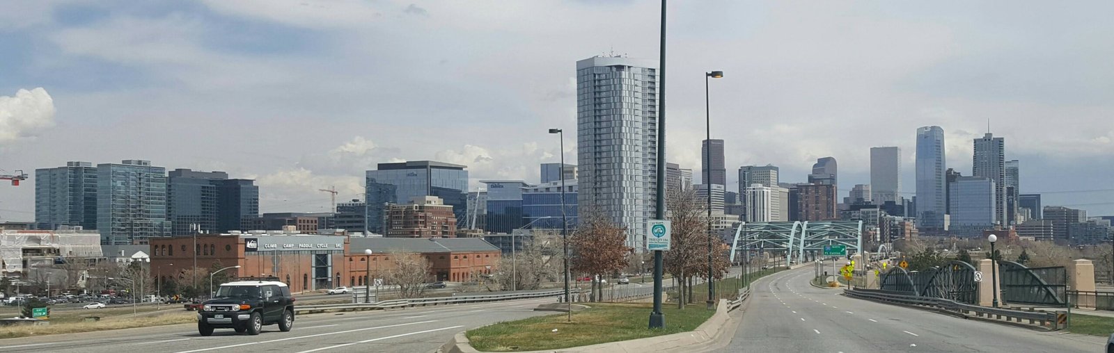 Denver downtown skyline daytime view across a bridge with passing SUV and bare winter trees