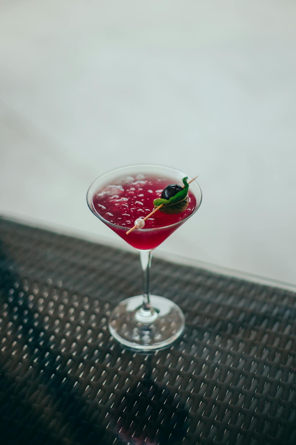 Deep red cherry colored cocktail in a martini glass with a basil and berry garnish, representative of the Dixie Elixir THC infused beverage line that launched in Colorado in 2010