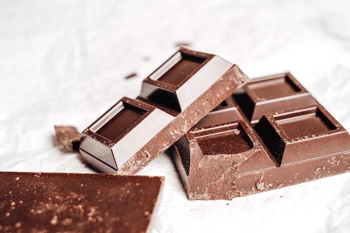 Stacked broken pieces of dark chocolate bars on a white background, representative of the Incredibles handcrafted high-grade cannabis oil chocolate bar line that has won Cannabis Cup placements since 2013