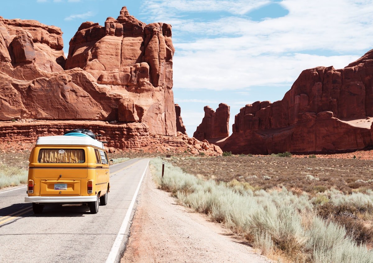 Yellow vintage van on a desert highway flanked by red rock formations evoking the Lebowski driving sequences scored by Kenny Rogers