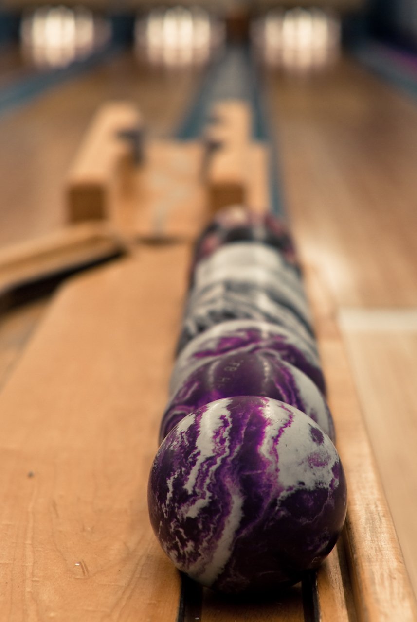 Row of purple and white marbled bowling balls in a return rack evoking the Jesus Quintana introduction sequence