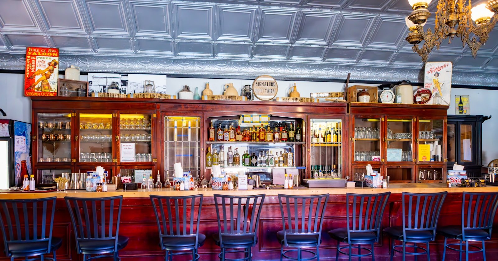 Old wooden saloon bar with vintage tin ceiling and stools evoking the Strangers closing voiceover at the bowling alley bar