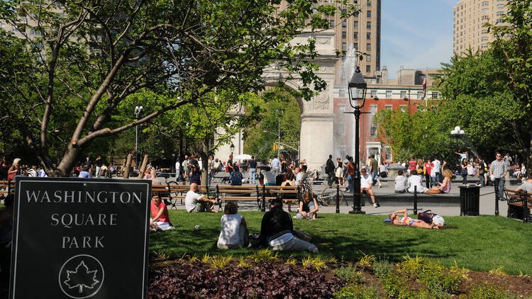 Washington Square Park arch and fountain in Greenwich Village, Manhattan, with people relaxing on benches and grass