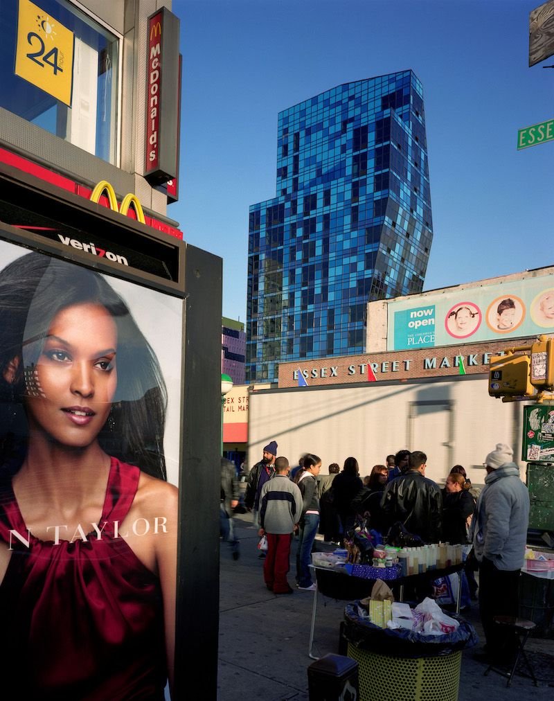 Lower East Side Manhattan street scene at Essex and Delancey with the Essex Street Market and a glass-tower backdrop