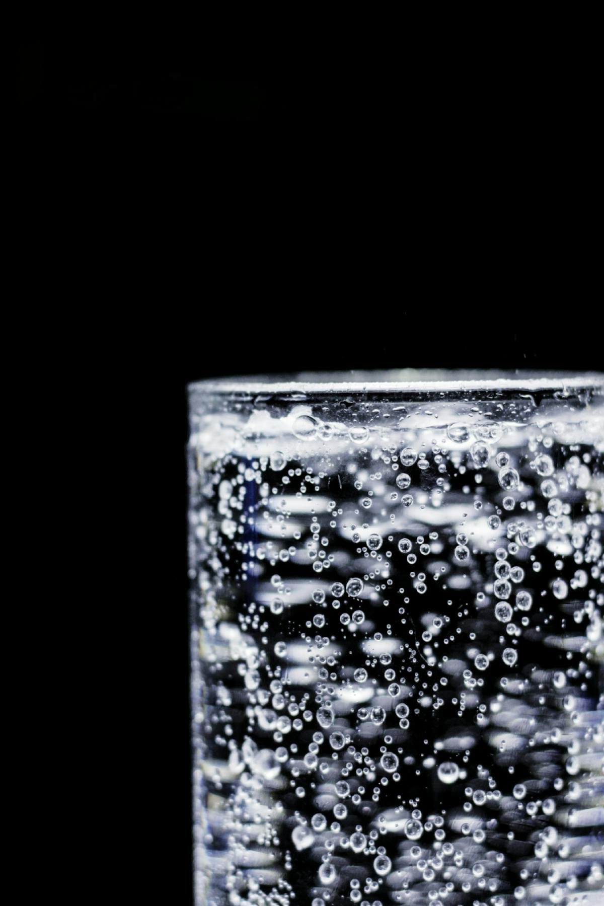 Glass of sparkling water with carbonation bubbles against a black background, representative of the Ripple by Stillwater dissolvable powder line that mixes invisibly into any beverage