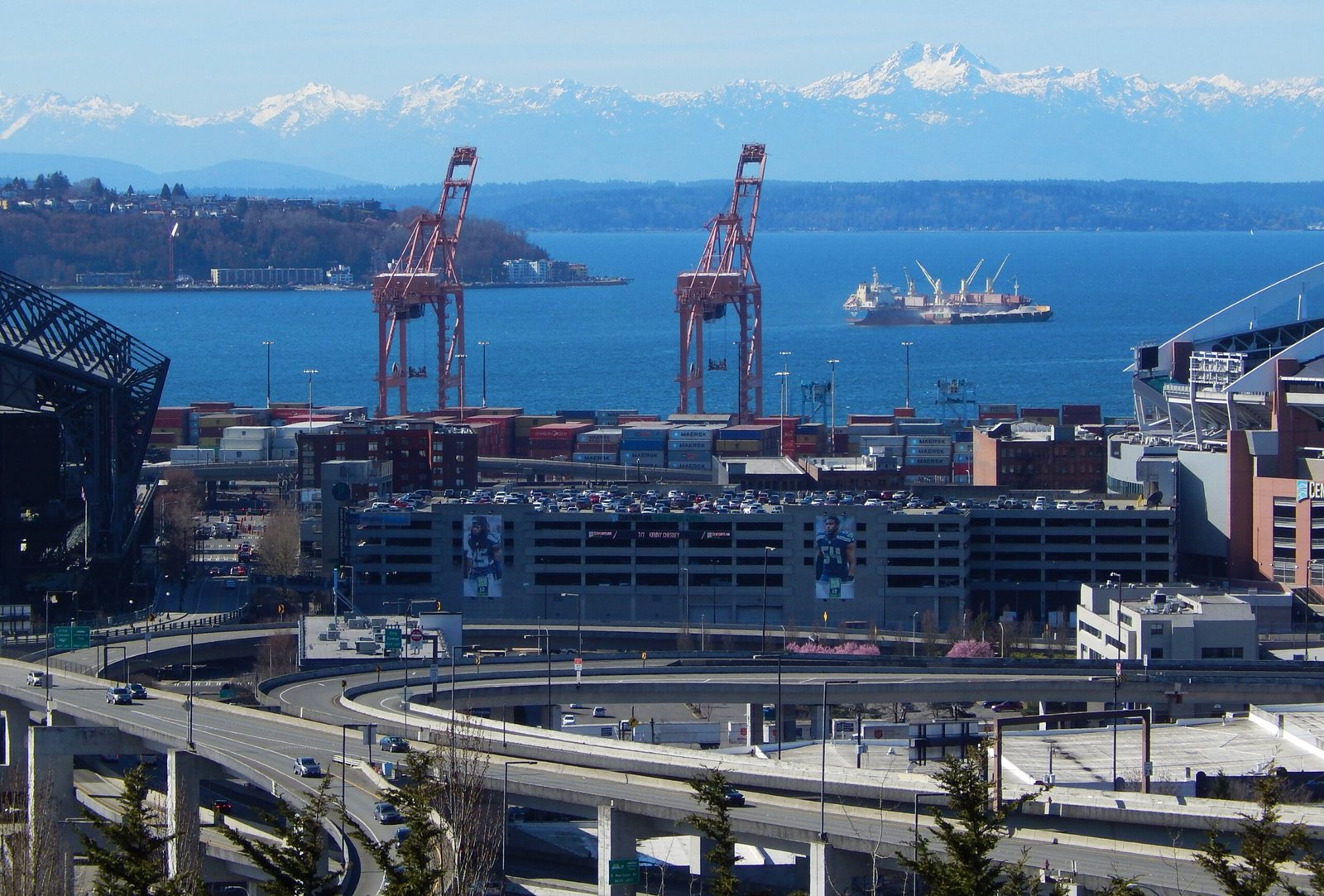 View of Seattle SODO industrial district from Jose Rizal Park, with Port of Seattle cranes, container yards, the elevated viaduct, and the Olympic Mountains across Elliott Bay