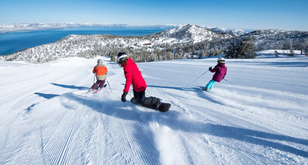 Skiers and snowboarders descending Heavenly Mountain Resort with Lake Tahoe in the background