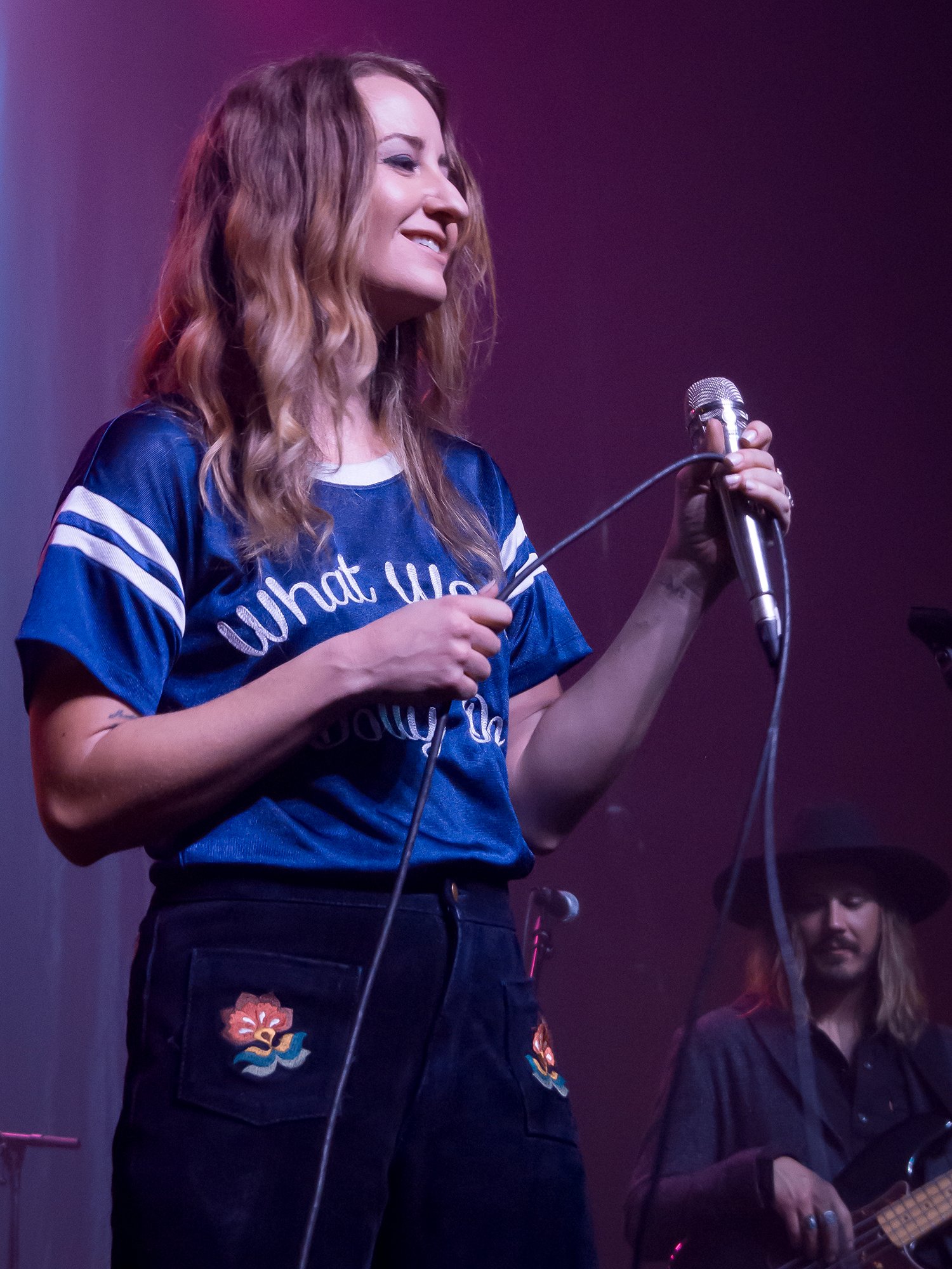 Margo Price performing on stage in a blue Dolly Parton tribute jersey holding a microphone, the Nashville songwriter who launched her own hemp CBD line in 2020 after years of cannabis advocacy