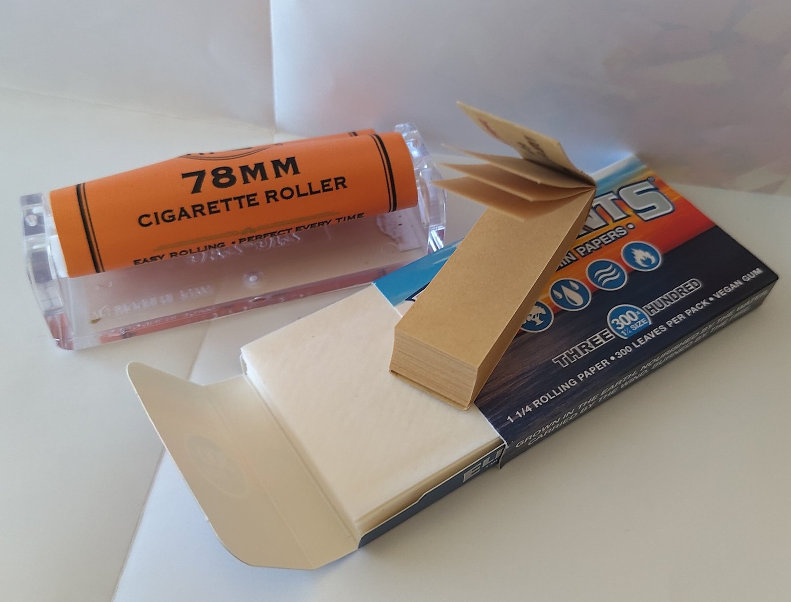 Joint rolling equipment laid out: cannabis, rolling papers, grinder, and crutch tips on a white surface
