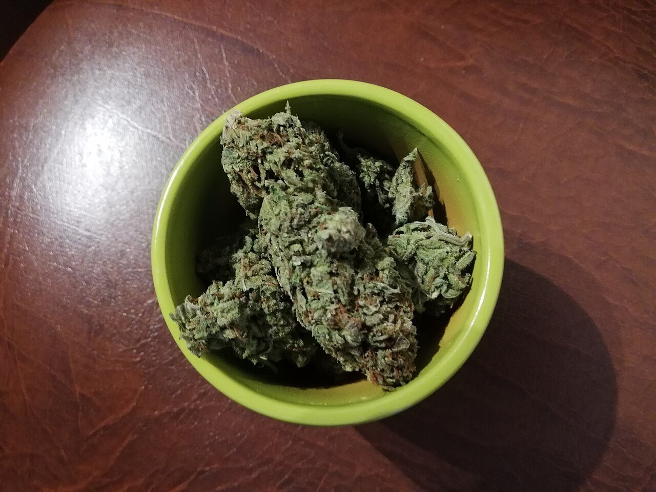 Cured cannabis buds with visible trichomes and orange pistils in a small bowl