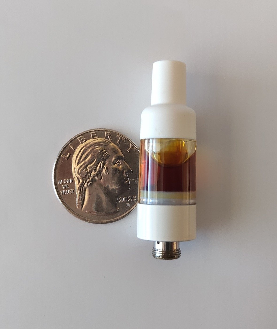 Single 510-thread cannabis oil cartridge with amber live resin next to a US quarter for scale