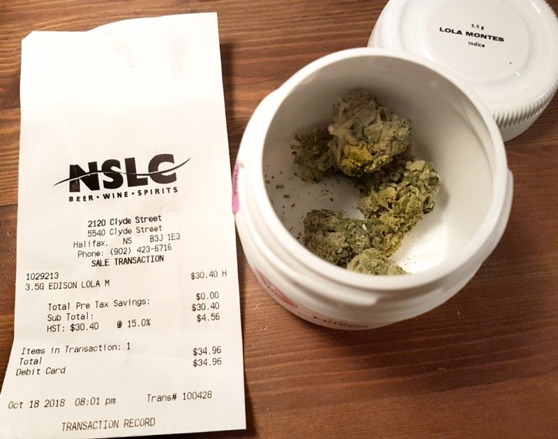 An open 3.5 gram plastic canister of cannabis flower beside a dispensary receipt