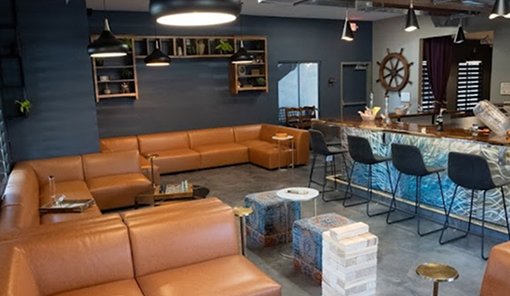 Wheelhouse Venice consumption lounge with brown leather sofas, nautical ship-wheel decor, and a bar area