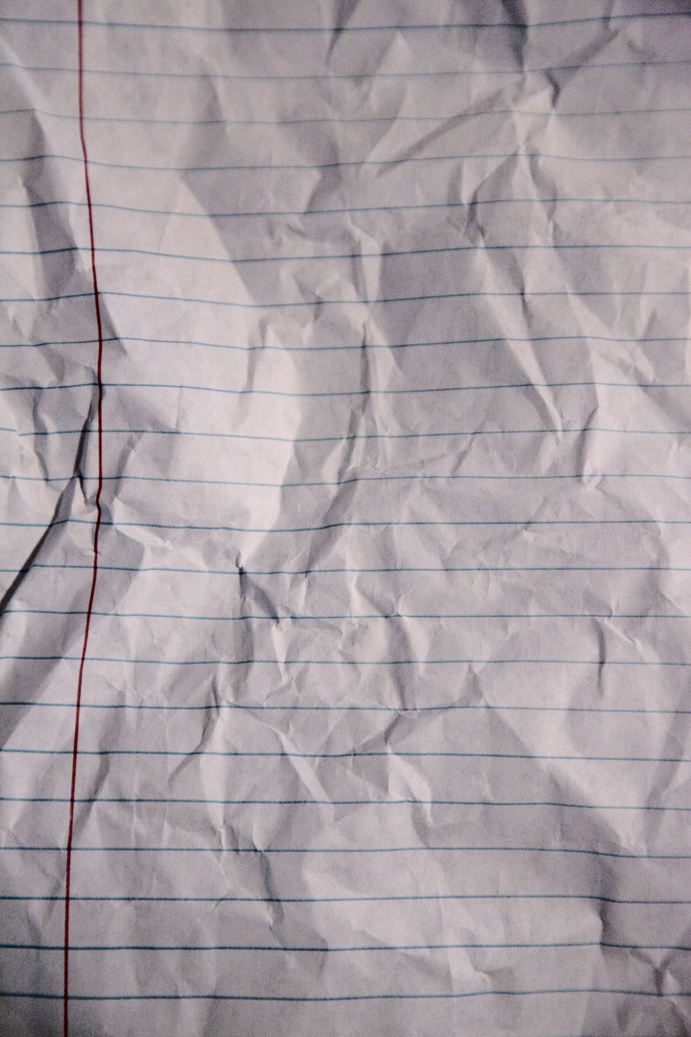 Wrinkled sheet of lined notebook paper showing blue ruling lines and red margin